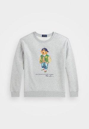 Sudadera gris con un oso impreso que viste una chaqueta varsity verde y jeans azules, con un cuello redondo y puños acanalados.