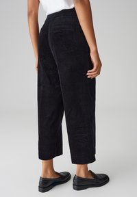 Black corduroy wide-leg pants with a textured finish, featuring pockets and a cropped length, paired with black loafers.