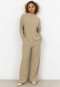 Beiges, geripptes Strickoberteil und weite Hosen-Set, das mit einem hohen Kragen, lockerem Schnitt und weicher Textur ausgestattet ist. Minimalistisches Design mit dezenten Details.