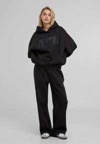 Schwarzes Hoodie- und Jogginghosen-Set mit einer geräumigen Kapuze, lockerer Passform und einem Fronttextdetail aus Strasssteinen. Weicher, texturierter Stoff.