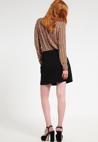 Langärmlige Bluse mit geometrischem Muster in Erdtönen, kombiniert mit einem schwarzen Rock. Verfügt über hochhackige Sandalen und eine glatte Textur.