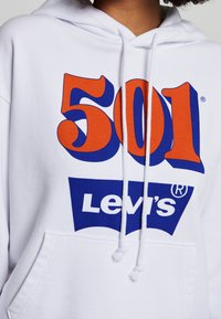 Vit sweatshirt med huva, med stort orange "501"-tryck och en blå Levi's-logga. Inkluderar en framficka och dragsko.
