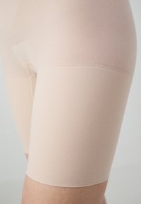 Beige taille-lange vormende shorts gemaakt van gladde, rekbare stof. Kenmerkt zich door een naadloos ontwerp en een lichte glans, nauwsluitend op het lichaam.