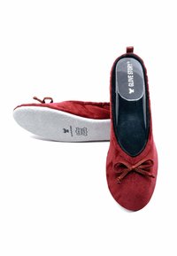 Ballerines en suède rouge avec un bout arrondi, un détail en nœud en dentelle et une semelle intérieure rembourrée. La semelle est texturée et de couleur gris clair.