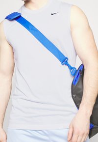 Light gray sleeveless athletic top with a small black logo, paired with a black crossbody bag featuring a blue strap and zipper accents.