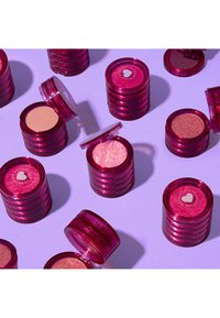 Pinoissa pyöreitä astioita läpikuultavasta fuksia muovista, joista osassa on kirkkaat kannet. Sisältää erilaisia sävyjä puristettuja puuterituotteita vaalealla taustalla.