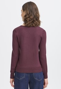 Burgunderfarbener Strickpullover mit langen Ärmeln und Rundhalsausschnitt, mit gerippten Bündchen und Saum, getragen mit dunklen Jeans.