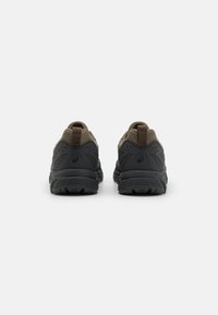 Sapatilhas pretas e castanhas com um upper de tecido texturizado, solas de borracha resistentes e um laço na parte de trás para facilitar o calçar.