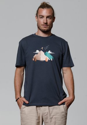 Navyblaue Baumwoll-T-Shirt mit einem Grafikdesign von Bergen, Bäumen und Wolken in Pastellfarben, runder Ausschnitt und kurzen Ärmeln.