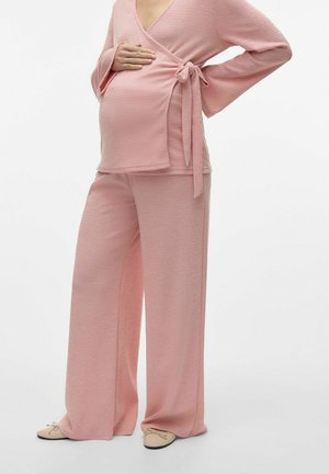 Haut de maternité rose avec manches longues et détail noué à la taille, associé à un pantalon rose à jambes larges et des chaussures plates.