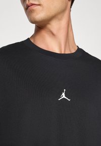 Crna pamučna majica s crew izrezom i malim bijelim Jumpman logom na prsima. Glatka tekstura s kratkim rukavima.