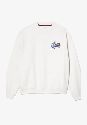 Sudadera blanca con escote redondo y puños de canalé. Presenta un parche impreso colorido en el pecho con varios diseños gráficos.