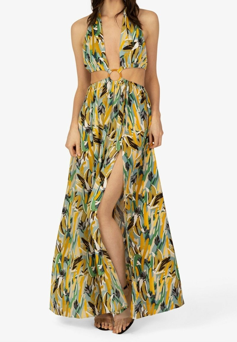 Femme portant une robe maxi sans manches, à motifs colorés, avec un décolleté en V profond, un détail en anneau à la taille et une fente haute à l'avant.