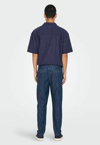 Cămașă navy cu manecă scurtă, cu guler pliabil, asociată cu pantaloni jeans închis la culoare, cu un croi lejer și buzunare pe spate.