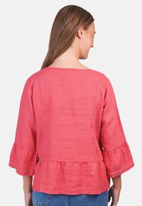 Korallefarbene Leinenbluse mit dreiviertellangen Glockenärmeln, ausgestattet mit einem Peplum-Saum und zarter Spitzeneinfassung entlang der Ärmel. 