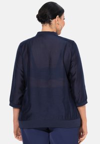 Laivansinis, kevyt pusero, jossa on kolme neljännestä hihoista, hieman läpikuultava rakenne ja pyöreä helma. Siinä on yksinkertainen kaulus ja elastiset hihansuut.