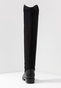 Bottes noires montantes jusqu'au genou avec une tige en tissu mat et lisse et un bout ainsi qu'un talon en cuir brillant. Caractérisées par un bout arrondi et un talon bloc bas.