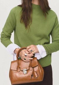 Sac à main en cuir marron au design structuré, avec une anse supérieure et des détails en métal argenté. Le modèle porte un pull vert avec des poignets blancs.