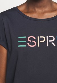 Camiseta azul marino con cuello redondo y mangas cortas. Presenta letras de colores en bloque que deletrean "ESPRIT" en rosa, verde y azul.