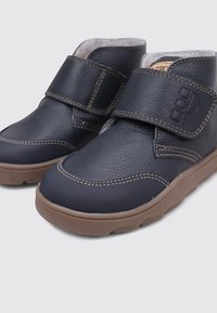 Zapatos de cuero de color azul marino oscuro con un acabado texturizado, que cuentan con una correa de velcro y una suela de goma de color marrón claro, diseñados para la comodidad y la durabilidad.
