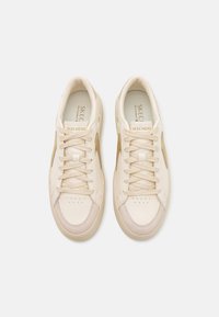 Un paio di sneakers Skechers beige e crema con lacci, punte in suede e dettagli dorati ai lati, viste dall'alto su uno sfondo bianco.