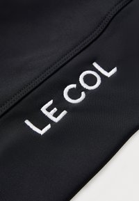 Schwarzes Fahrradjacket mit weißen gestickten Text "LE COL", mit glatter Textur und minimalistischem Design. Genähte Akzente entlang der Kanten.