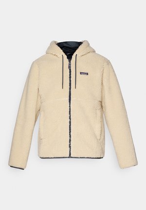 Cream-colored fleece jacket with a hood, textured fabric, front zipper, and two side pockets. Features dark trim and a logo patch.