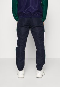 Námořnické tepláky s elastickým pasem a manžetami, se zelenými a bílými bočními panely. Vyrobeno z hladkého, lehkého materiálu.