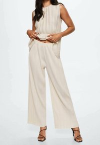 Béžová plisovaná bezrukávová blůza s krátkým lemem, spárovaná s odpovídajícími širokými kalhotami s bočními kapsami a texturovanými detaily.