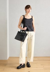 Musta satiininen kamisolipaita säädettävillä olkaimilla, kermaiset leveälahkeiset housut ja paksupohjaiset mustat loafersit. Asusteena: jämäkkä musta käsilaukku.