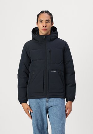 Chaqueta acolchada negra con capucha, que cuenta con dos bolsillos frontales con cremallera y un logo en la parte inferior izquierda. Tejido suave, diseño acolchado y puños elásticos.
