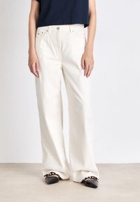 Bredde ben, elfenbensfarvet denimbukser med subtil tekstur, høj talje og forreste lommer. Sammen med sorte flade sko med dekorative detaljer.