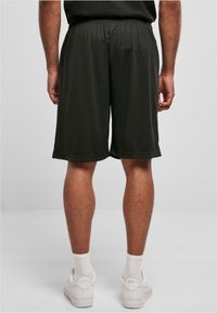 Shorts de sport noirs avec une taille élastique, texture lisse, longueur au genou et un design simple. Portés avec des baskets blanches et des chaussettes.