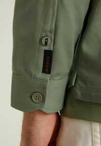 Groene katoen twill jas mouw met knoopsluiting en merklabel. Soepele textuur met een op maat gemaakte manchetontwerp.