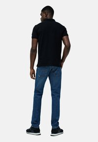 Camisa polo negra, jeans azules y zapatillas negras. La polo tiene un cuello con solapa. Los jeans tienen un corte recto con bolsillos traseros.