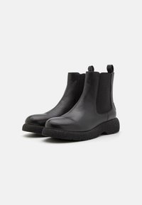 Botas Chelsea de cuero negro con suela de goma texturizada, paneles elásticos en los laterales y tiradores traseros para facilitar su uso.