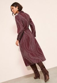 Bordo suknelė su balta bangų raštu, diržo juosta, ilgos rankovės ir apykaklė. Suderinta su rudomis zomšinėmis ilgaaulių batais ant kulno.