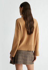 Maglione oversize color cammello con orlo e polsini a costine, abbinato a una gonna a quadri marrone. Morbido al tatto e dalla vestibilità comoda.