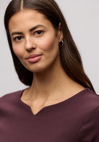 Prążkowany top z dekoltem w serek w głębokim odcieniu bordo. Miękka faktura z dopasowaną sylwetką, z gładkim dekoltem i subtelnymi detalami szwów.