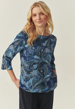 Tmavomodrý dlhý rukáv s víriacim kvetinovým vzorom v svetlejších modrých odtieňoch. Zaoblený výstrih a bočné vrecká. Pohyb jemnej tkaniny.