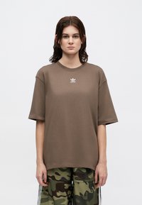 Tricou oversize maro din bumbac, cu guler rotund, mâneci scurte și un mic logo alb adidas pe piept.