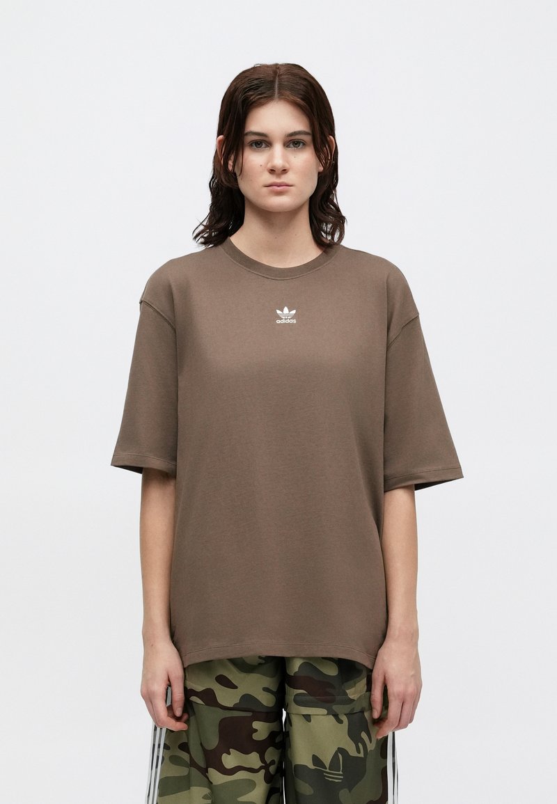 Braunes oversized T-Shirt aus Baumwolle mit Rundhalsausschnitt, kurzen Ärmeln und kleinem weißen adidas-Logo auf der Brust.