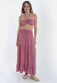 Completo due pezzi rosa con top bandeau arricciato e gonna maxi a strati con vita smock. Indossato con sandali intrecciati slip-on.
