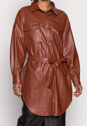 Brązowa sukienka koszulowa z długim rękawem ze sztucznej skóry, z paskiem, zapinana na guziki, z dwoma kieszeniami na piersi i spiczastym kołnierzykiem, noszona przez osobę.