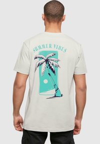 Light beige t-shirt featuring a graphic of a palm tree and sun in teal and black. Text reads "SUMMER VIBES" above the design.