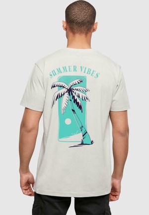 Hellbeige T-Shirt mit einem Grafikdesign von einer Palme und einer Sonne in Teal und Schwarz. Der Text "SUMMER VIBES" steht über dem Design.