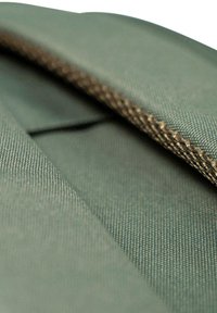 Groene textielproduct met een gladde textuur, diagonale stiksels en een contrasterende tan draad langs de rand.