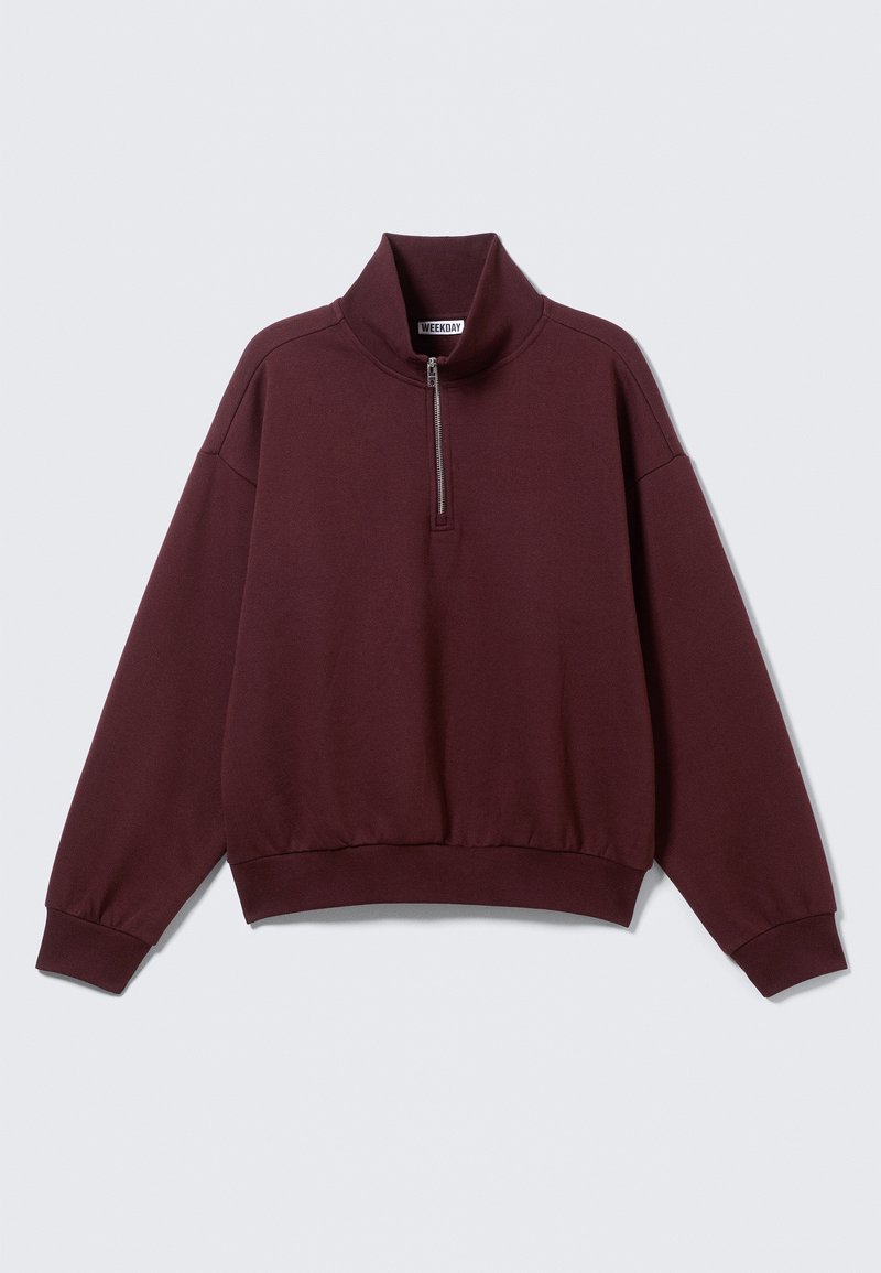 Burgundiapunane pusaga pullover, millel on kõrge kaelus ja pooleldi lukuga sulgur. Omadusteks on pikad varrukad ja lõdvestunud istuvus, mida täiustavad soonilised mansetid ja alumine äär.