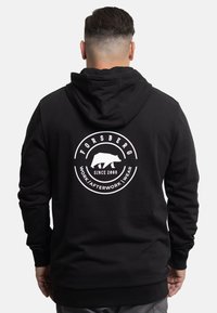 Black hoodie made of cotton blend, featuring a large circular white logo with a bear and text on the back. Includes a drawstring hood.