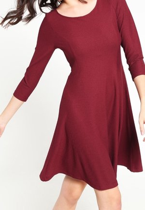 Robe en tricot bourgogne avec un décolleté arrondi, des manches trois-quarts et une silhouette évasée. Présente un tissu texturé pour plus de profondeur.